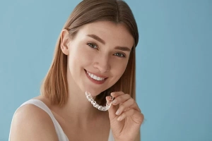 young woman holding an Invisalign clear aligner near her mouth