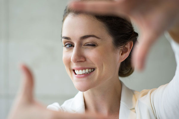 middle aged woman smiling while holding her hands as if taking a photo