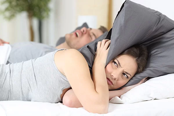 woman covering her ears with a pillow to block out her partner's loud snoring