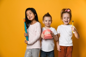 three kids holding giant versions of a teeth model and toothbrushes